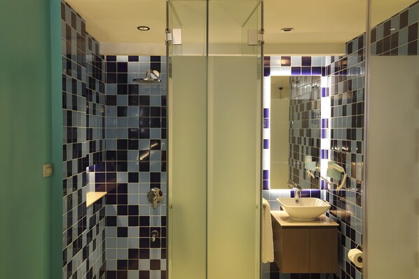 A bathroom with a glass door, a sink with a mirror, and a toilet. - Lagùn Hotel (El Nido)