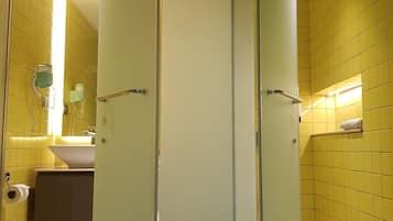 Un baño con paredes de azulejos amarillos, un lavabo blanco y una cabina de ducha de vidrio.