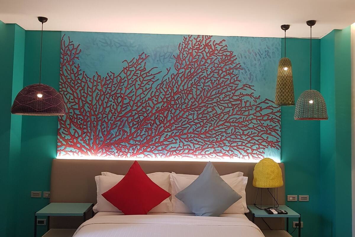 A modern bedroom with a large bed, teal walls, and a coral reef mural.