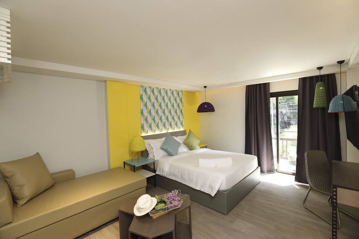 A modern hotel room with a bed, a sofa, a desk, and a chair.