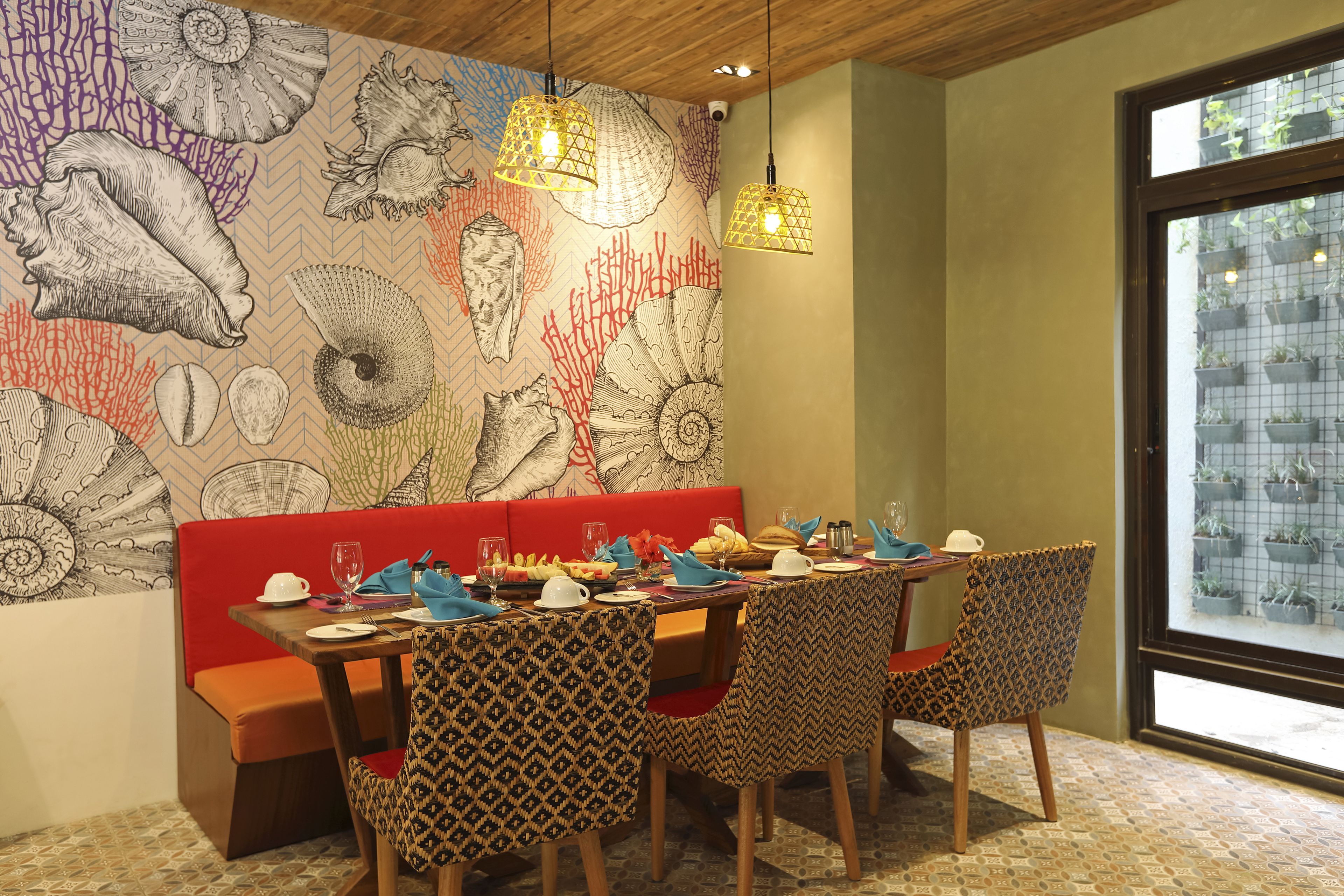 A dining area with patterned chairs, a red bench, and a wall mural of shells and corals.