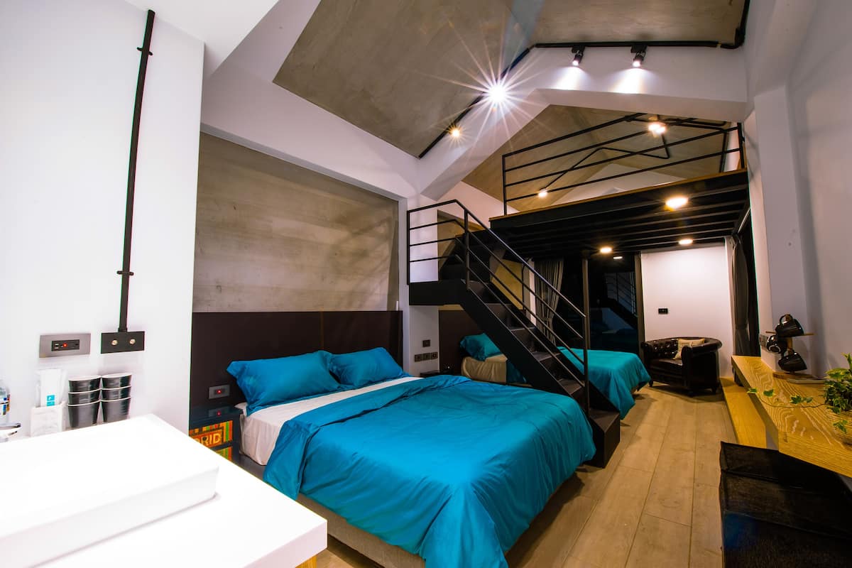 A modern hotel room with a large bed, a desk, and a staircase leading to an upper level.
