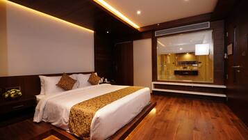 Habitación de hotel con una cama grande, suelo de madera, un banco empotrado y vista al interior del hotel.