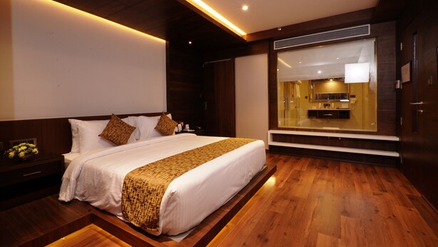 Habitación de hotel moderna con una cama grande, suelo de madera y vista de la cocina a través de un panel de vidrio.