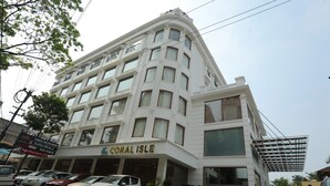 Un hotel de varios pisos llamado "Coral Isle", con un diseño arquitectónico moderno, que presenta una entrada destacada y varios coches aparcados al frente.