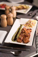 A dining table with a white rectangular plate containing grilled chicken, a green sauce, and a side salad.