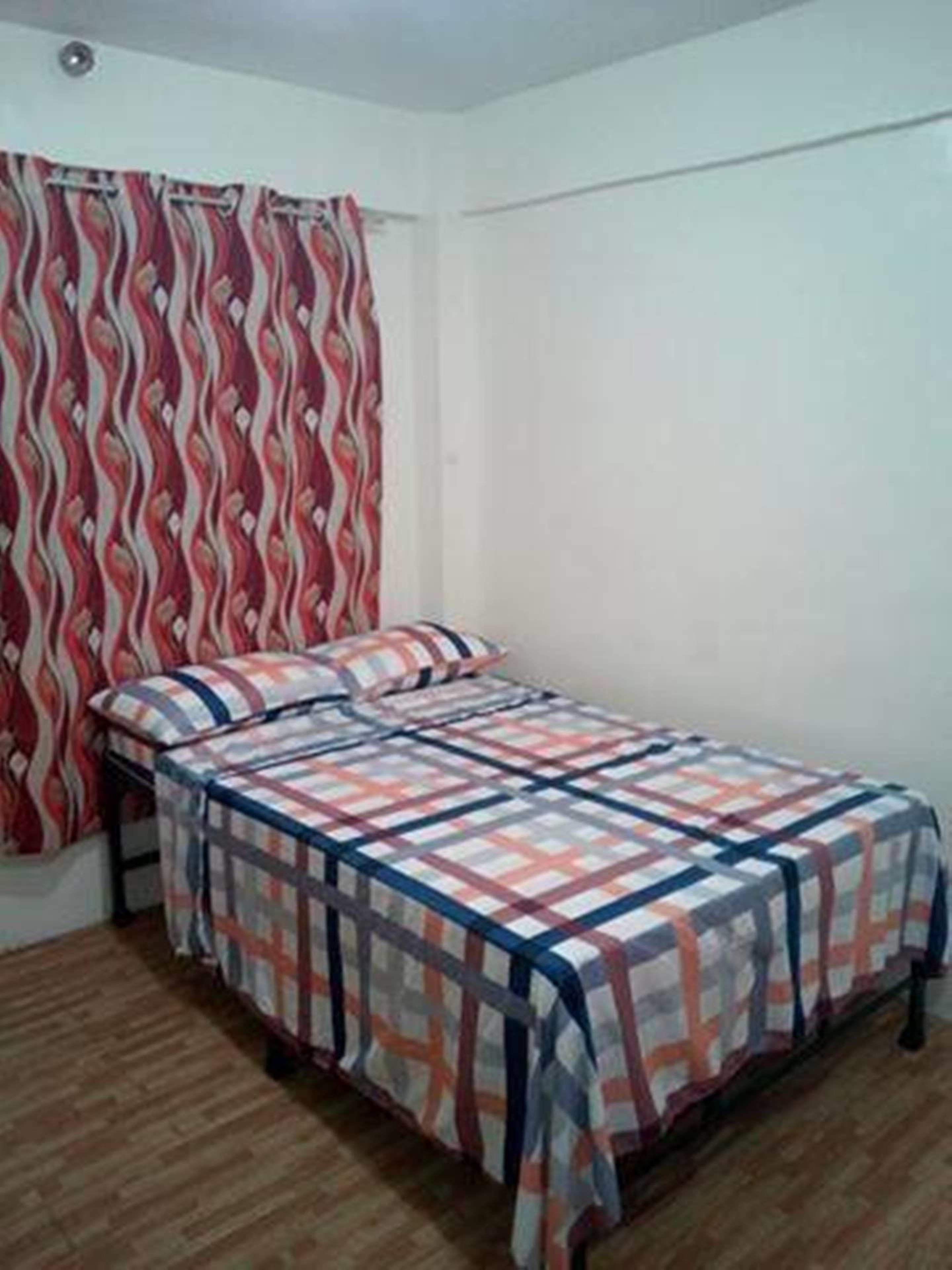 A single bed with a patterned bedspread, a bedside table, and a curtain with a wavy design.