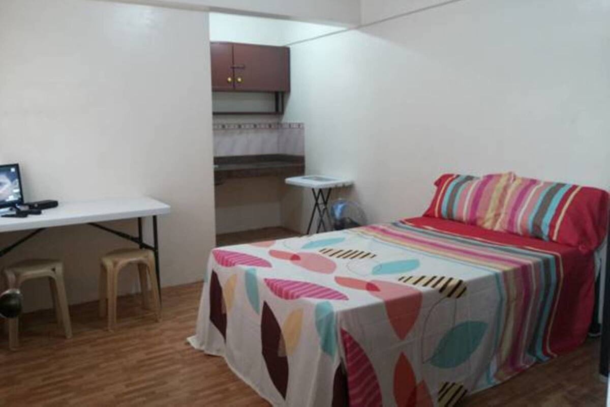 A small, compact room with a bed, a desk, and a kitchenette.