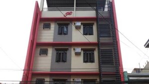 Un edificio de varios pisos con fachada roja y color crema, que muestra un cartel de unidad de alquiler.