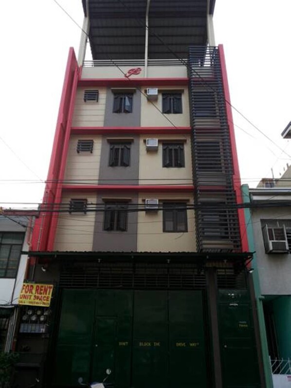 A multi-story building with a red and beige facade, featuring a sign for a rental unit space.