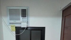 Habitación de esquina con ventilador de pie, equipo de aire acondicionado y puerta de madera.