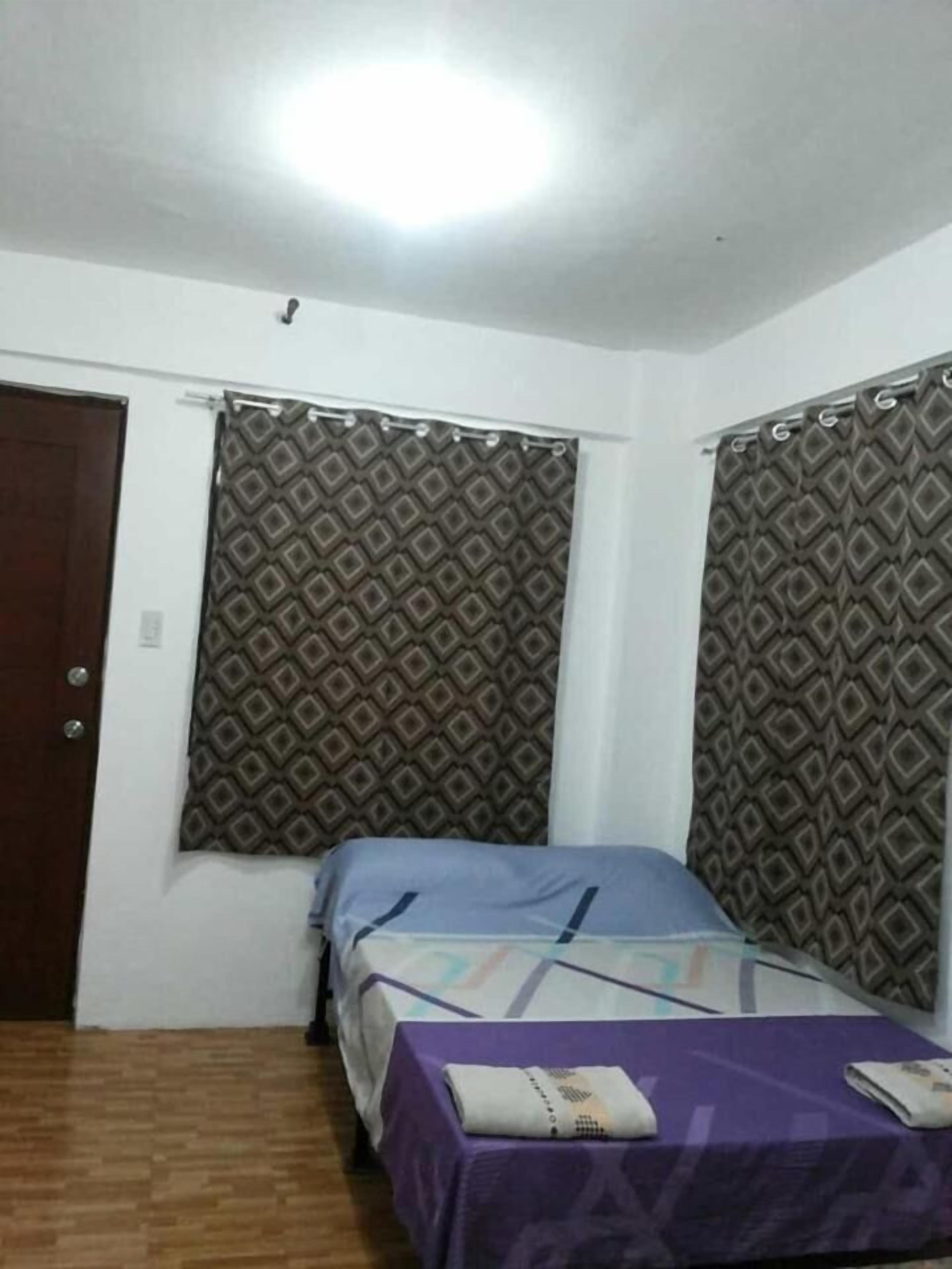 A small, simple room with two beds, a wooden floor, and patterned curtains.