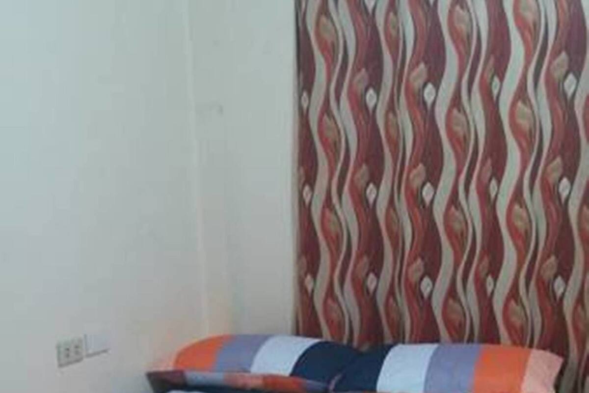 A single-bed room with a striped bedspread, a curtain with a wavy pattern, and a wooden floor.