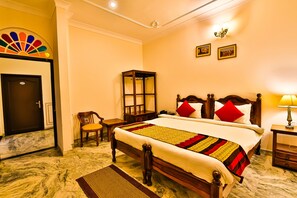 A hotel room with a marble floor, a wooden bed with red and white pillows, a wooden nightstand with a lamp, a wooden chair, and a wardrobe. - Harsoli Haveli by Rivaa- A Heritage Boutique Hotel (Jaipur)