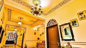 Um corredor com um candelabro, um sofá, uma porta e um espelho na parede.
