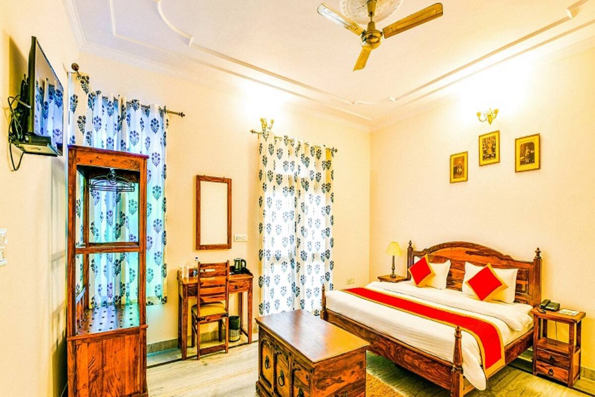 Una habitación de hotel con una cama de madera, un escritorio, una silla, un armario y un ventilador de techo.