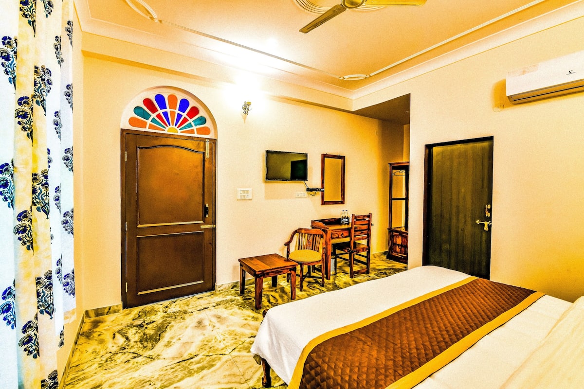 Una habitación de hotel con cama, escritorio, silla, televisor y puerta.