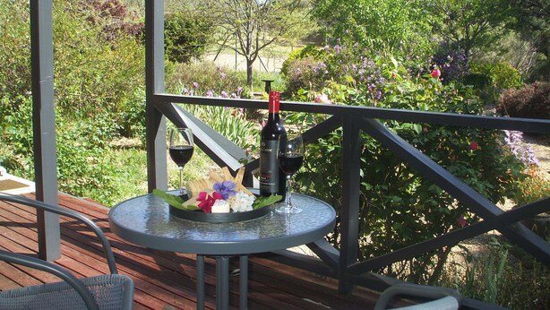 A wooden deck with a round table and chairs, a bottle of wine, and a glass on the table. - Archery Road Estate (Tanunda)