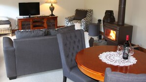A living room with a sofa, a table with a bottle and glasses, a TV, a lamp, and a fireplace. - Archery Road Estate (Tanunda)