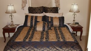 A bed with a patterned bedspread, two bedside tables with lamps, and a window with curtains. - Archery Road Estate (Tanunda)