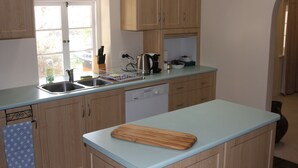 A kitchen with wooden cabinets, a dishwasher, a sink, and a cutting board on the countertop. - Archery Road Estate (Tanunda)