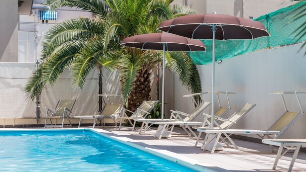 A swimming pool with lounge chairs and umbrellas. - Hotel Plaza (Cattolica)