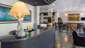 A hotel reception area with a marble floor, a reception desk, a statue, a painting, and a bar area in the background. - Hotel Plaza (Cattolica)