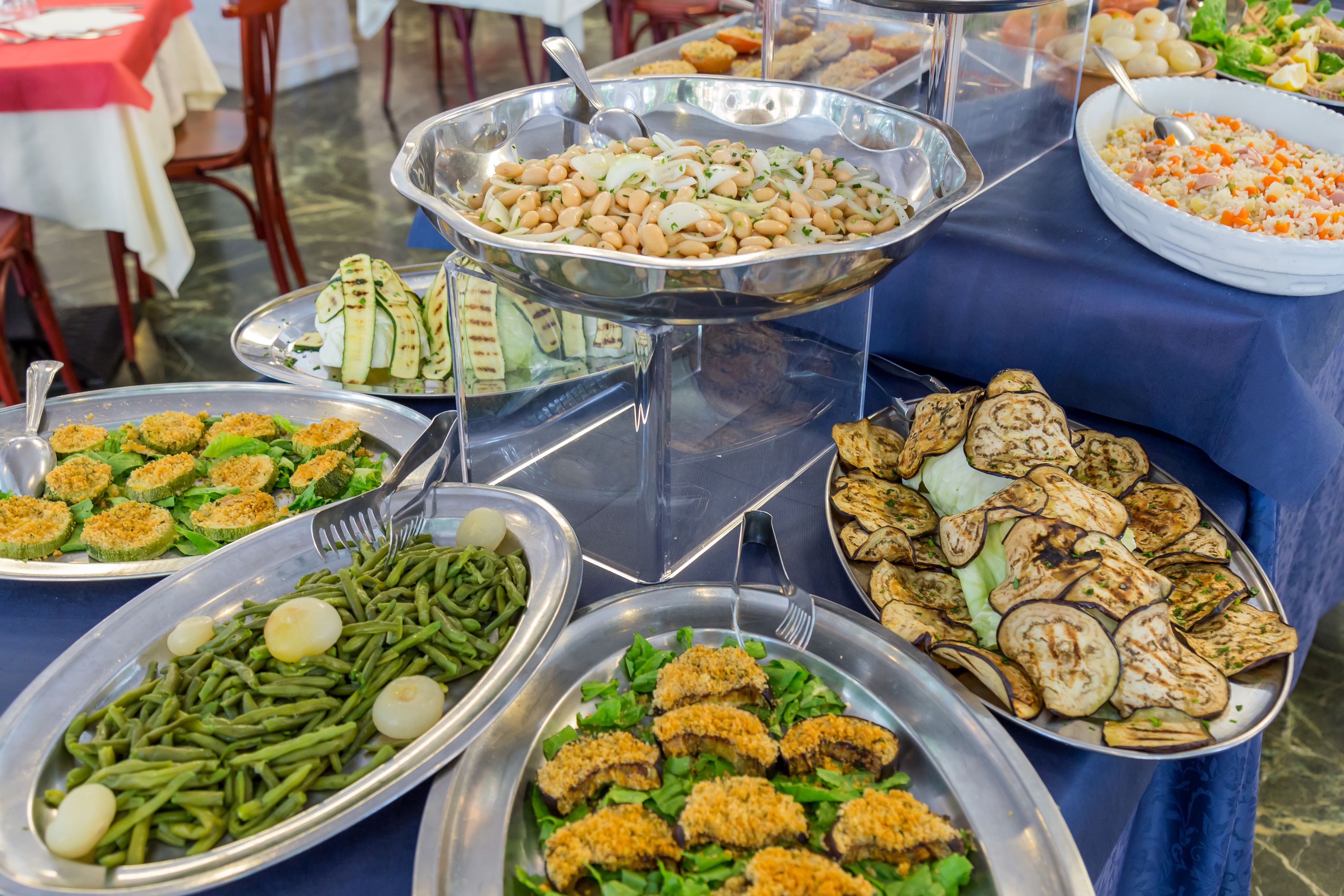 A buffet table with various dishes including beans, grilled vegetables, and salads.
