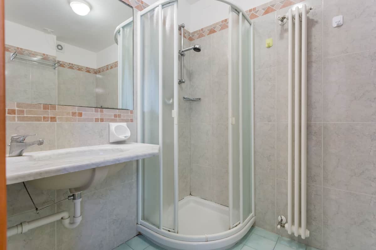 Ein modernes Badezimmer mit einer gläsernen Duschkabine, einem weißen Waschbecken und einem Fliesenboden.