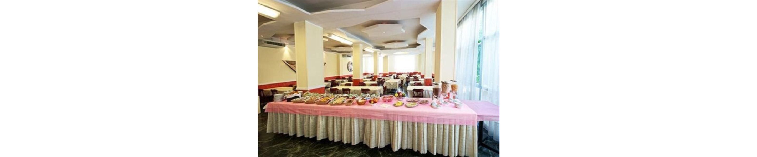 A banquet hall with tables set for a meal, featuring a pink tablecloth and white drapery.