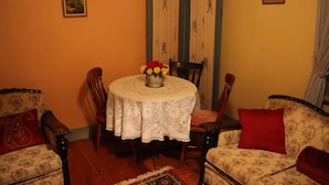 A dining area with a round table, floral centerpiece, patterned chairs, and a red cushion on a sofa. - Kookaburra Cottage (Burra)