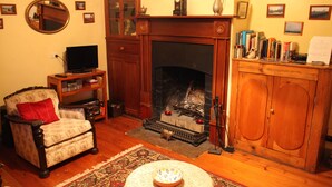 A cozy living room with a fireplace, a television, a bookshelf, and a comfortable armchair. - Kookaburra Cottage (Burra)