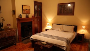 A bedroom with a large bed, two bedside lamps, a wooden dresser, a fireplace, and a rug. - Kookaburra Cottage (Burra)