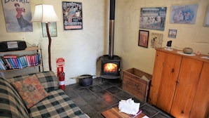 A cozy living room with a checkered sofa, a wooden table, a bookshelf, a fireplace, and vintage posters on the wall. - Griffiths Cottage (Burra)