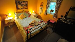 Een slaapkamer met een bed, nachtkastjes, een kaptafel, een raam met gordijnen, en een schilderij aan de muur.