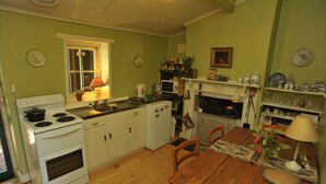 Een keuken met witte kastjes, een fornuis, een magnetron en een eettafel met stoelen.