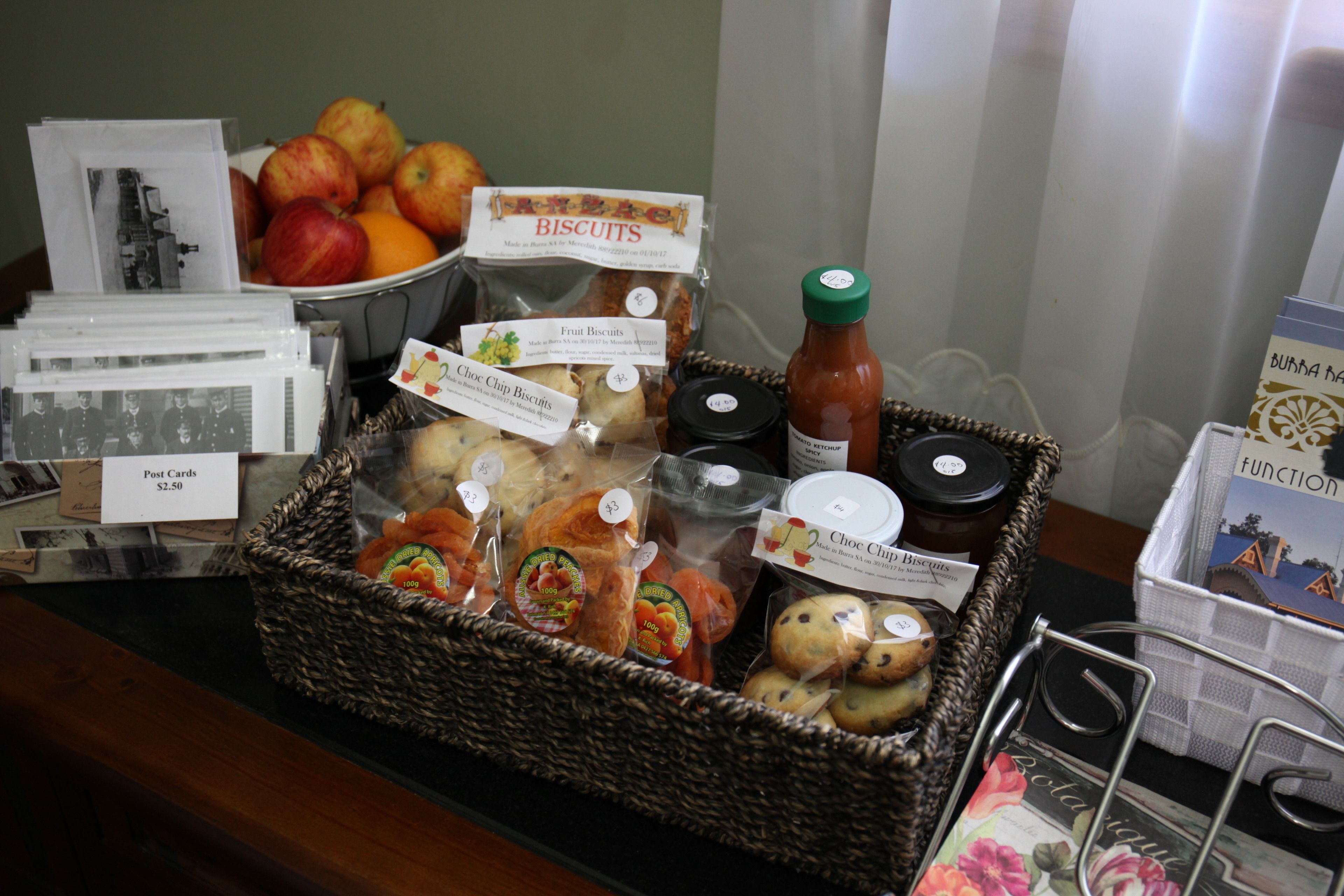 A display of assorted snacks and treats, including fruit, biscuits, and a bottle of sauce, arranged on a counter.