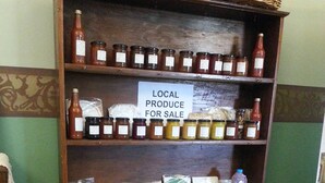 Un mueble de madera con frascos de productos locales a la venta, una cesta de mimbre y un cartel que anuncia la oferta.