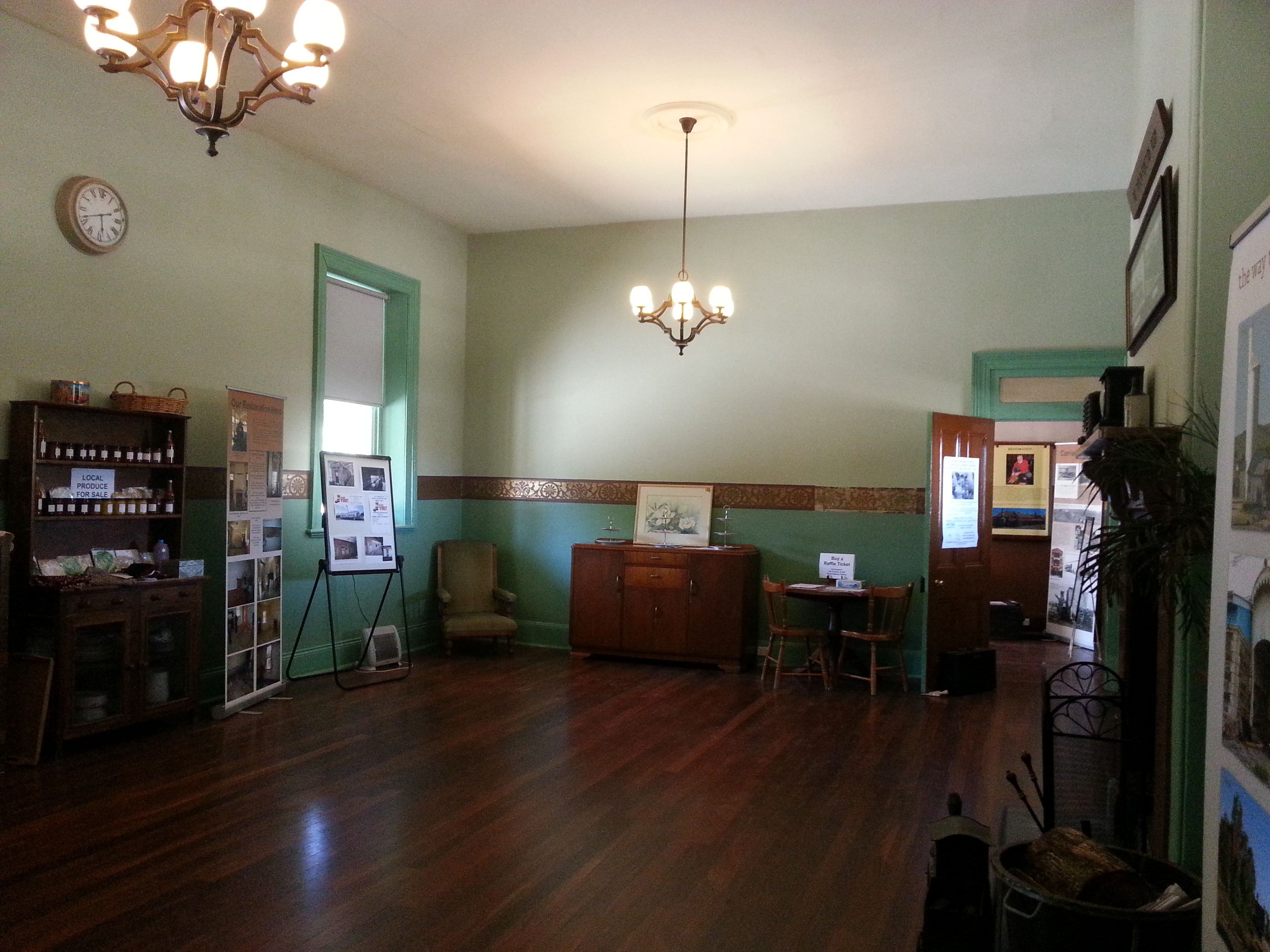 A room with wooden flooring, a chandelier, a clock, a bulletin board, and a cabinet with local produce for sale.
