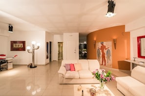 A living room with a beige sofa, a coffee table with flowers, a floor lamp, and a painting on the wall.