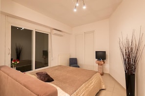 A bedroom with a bed, a sofa, a TV, and a sliding door to a balcony.