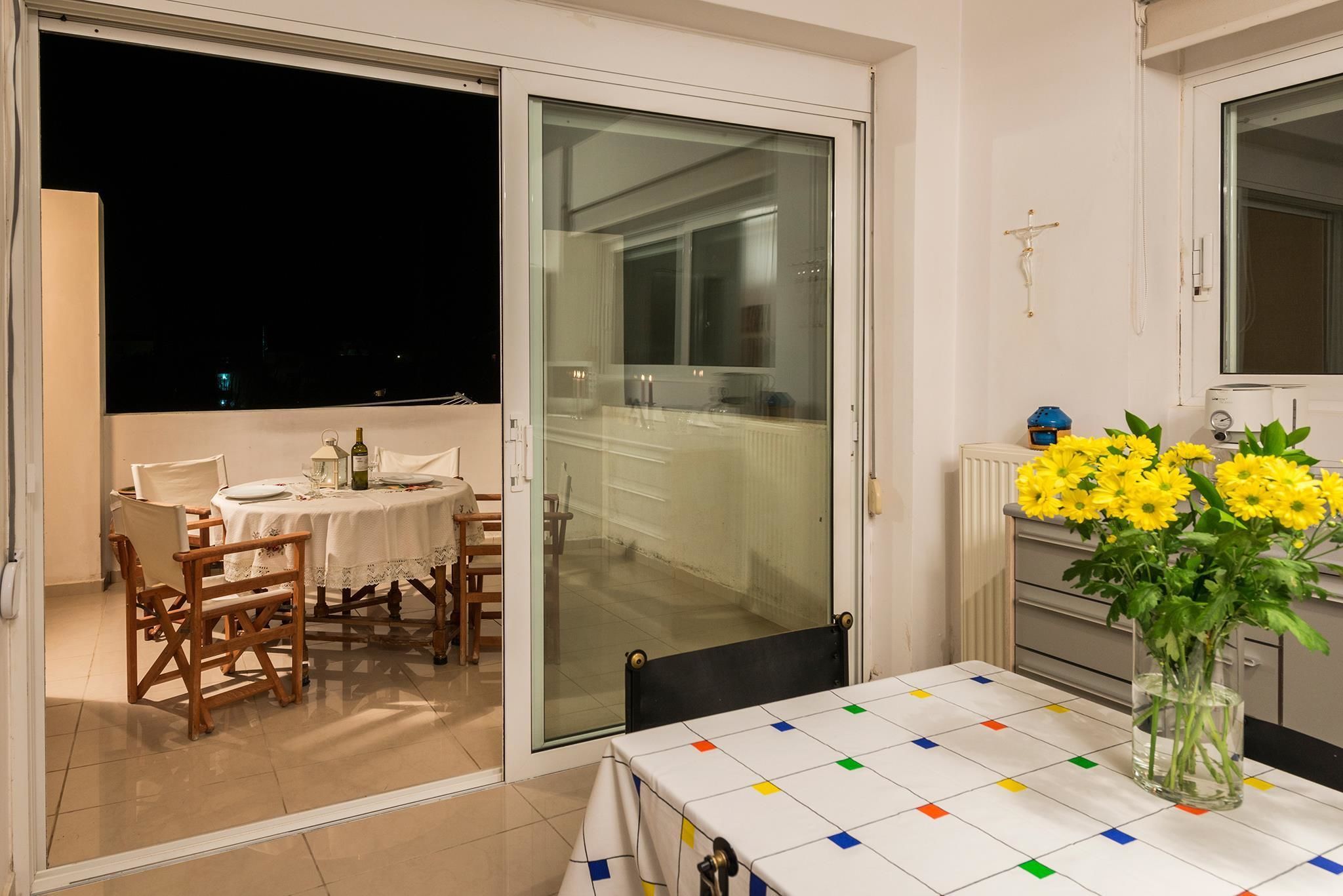 A dining area with a table set for two, a chair, and a vase of yellow flowers.