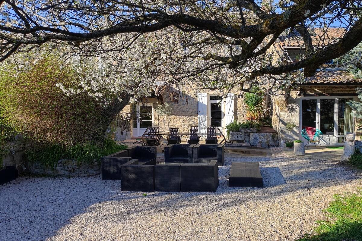 Un patio con mobiliario exterior, un edificio de piedra y un árbol grande.