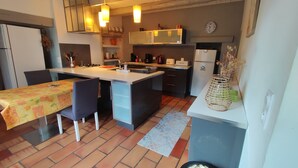 Une cuisine compacte avec un îlot central, une table à manger et des chaises. On y trouve un réfrigérateur, une cuisinière et divers appareils de cuisine.