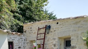 Un bâtiment en pierre avec une échelle en bois, des plantes en pot et une petite fenêtre.
