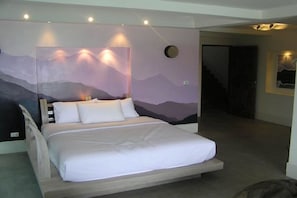 A bedroom with a bed, a headboard with a mountain mural, and a staircase in the background.