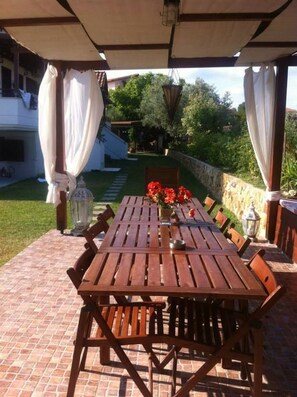 Un patio exterior con mesa y sillas de madera, rodeado de suelo de ladrillo y pared de piedra.