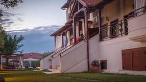 A two-story building with a balcony, a covered outdoor seating area, and a well-maintained lawn. - Xenonas Liogerma (Aristotelis)
