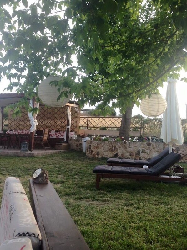 Un espacio de patio con un banco de madera, una silla de descanso y una zona de estar techada.
