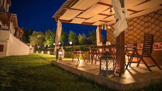 An outdoor patio area with tables and chairs, a lantern, and a pergola structure. - Xenonas Liogerma (Aristotelis)
